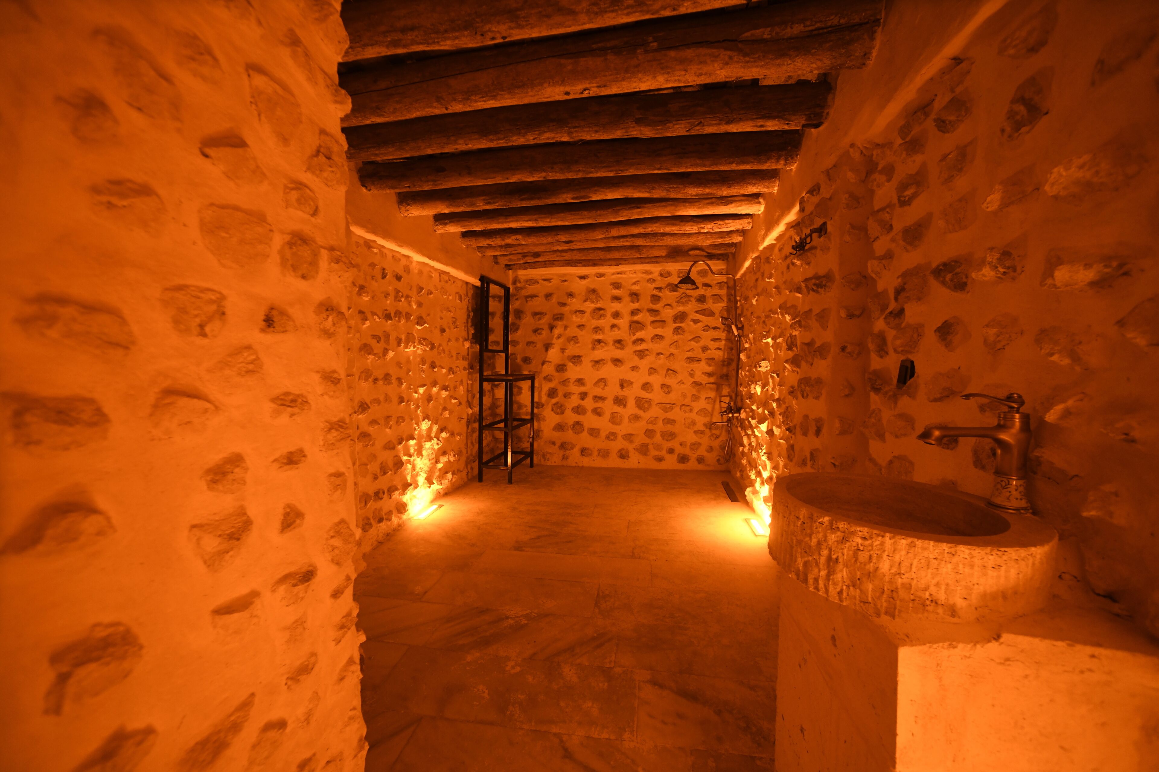 Un baño con paredes de piedra, techo de madera, un lavabo y una escalera apoyada en la pared.