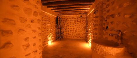 Un baño con paredes de piedra, techo de madera, un lavabo y una escalera apoyada en la pared.