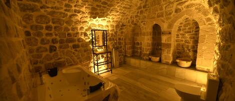 A stone-walled bathroom with a bathtub, a sink, and a shelf with toiletries.