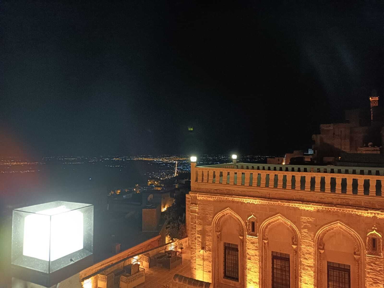A night view of a historic building with arched windows and a balcony overlooking a cityscape.
