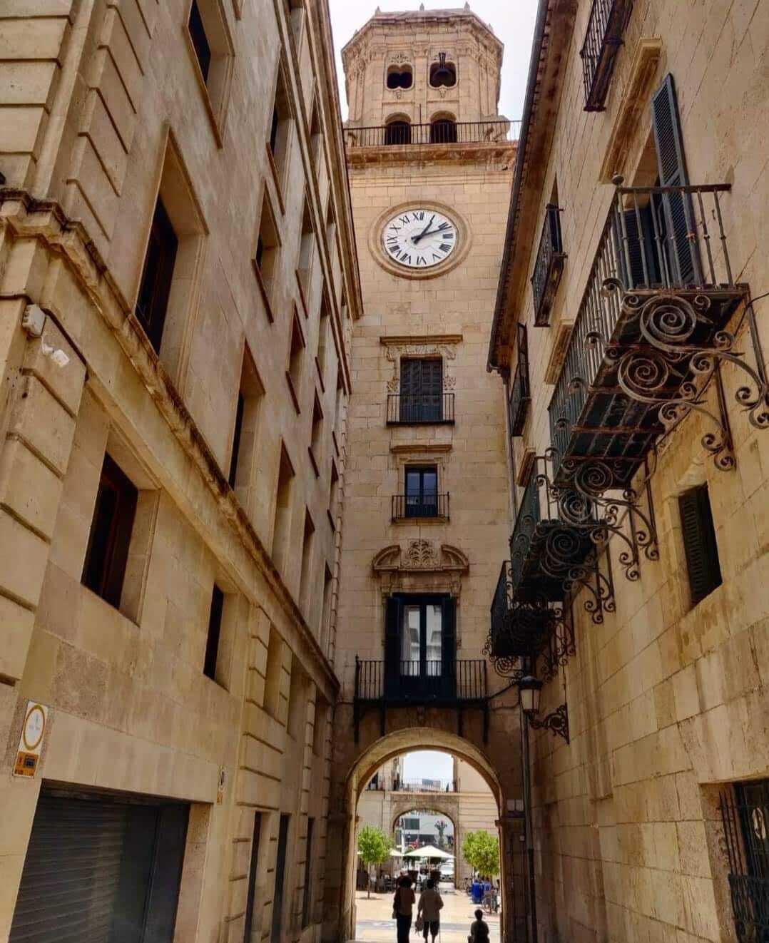 Un callejón estrecho con una torre de reloj y un gran reloj en el edificio.
