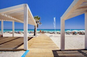 Un muelle de madera que da a una playa con estructuras blancas en lo alto.