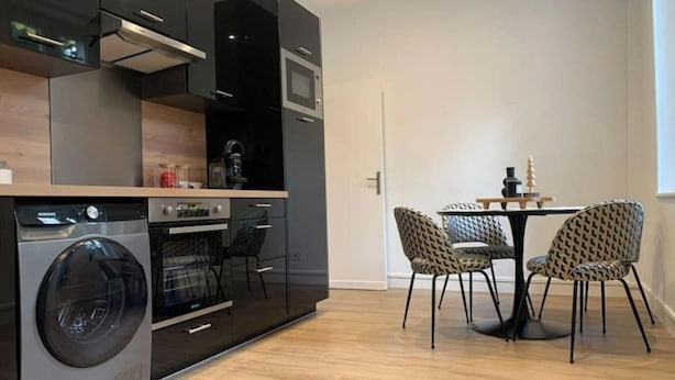 A compact kitchen with a washing machine, oven, and microwave. There is a dining area with a table and chairs.