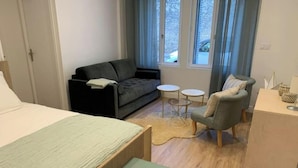 A modern hotel room with a bed, a grey sofa, a small round table, and a chair.