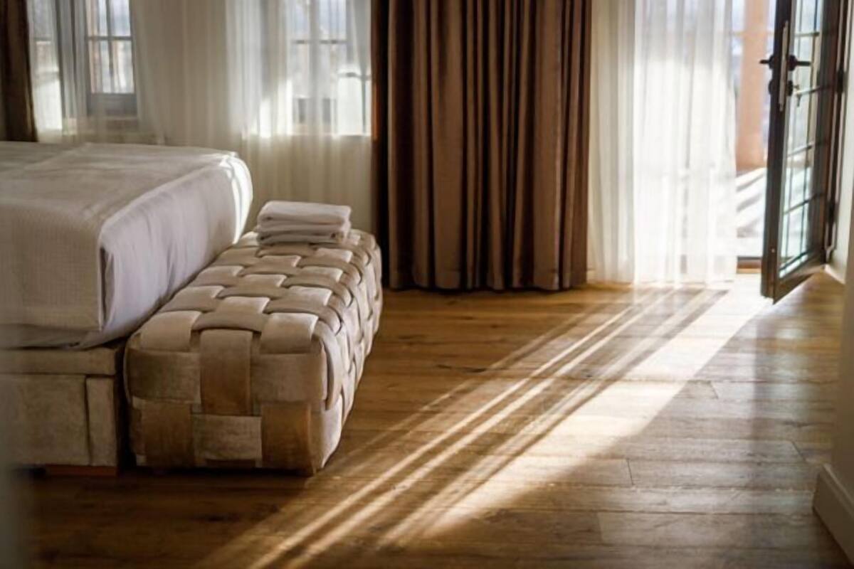 Quarto com cama grande, um banco e piso de madeira.