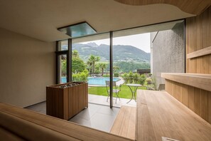 Une chambre moderne dotée d’une grande fenêtre, d’un banc en bois, d’une petite table et offrant une vue sur une piscine et des montagnes.