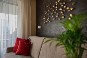 A living room with a sofa, red cushions, a wall-mounted light fixture, and a potted plant.