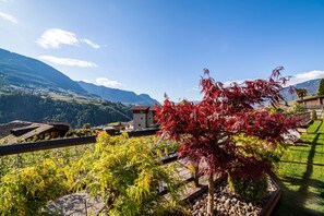 A mountainous landscape with a house and a tree with red leaves.