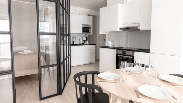 Une cuisine moderne avec des meubles blancs, un four à micro-ondes et un coin repas avec une table dressée pour six personnes.