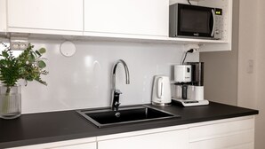 Une cuisine moderne avec un évier noir, un robinet en acier inoxydable, une machine à café Bosch et un four à micro-ondes placé au-dessus du plan de travail.