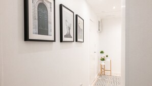 Un couloir avec trois tableaux encadrés accrochés au mur, une petite table sur laquelle est posée une plante et un sol à motifs.