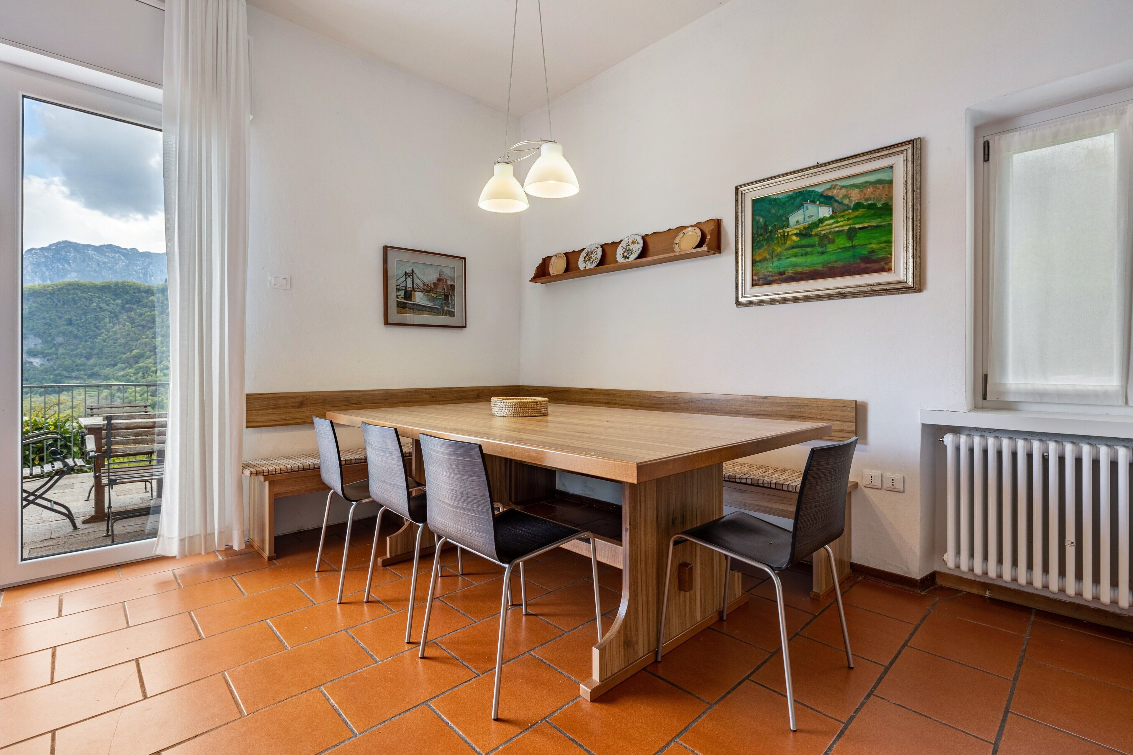 A dining area with a wooden table, four chairs, a hanging light fixture, and two framed pictures on the wall.
