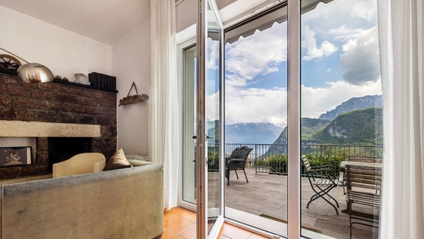 A living room with a sofa, a fireplace, and a sliding glass door leading to an outdoor patio with chairs and a view of mountains.
