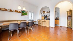 A modern kitchen with a dining area, featuring a wooden bench, bar stools, and a tiled floor.