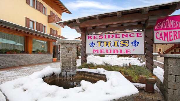 Une enseigne indiquant « Résidence Iris Meublée », avec un puits en pierre et de la neige tout autour.