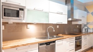 Een moderne keuken met een RVS magnetron, vaatwasser en oven, een houten aanrechtblad en witte kastjes.