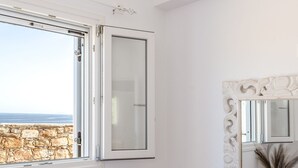 A bedroom with a large window, a mirror with an ornate frame, and a bed with a textured bedspread. - Kalliston, Romantic Villa with Amazing Sea View (Naxos)