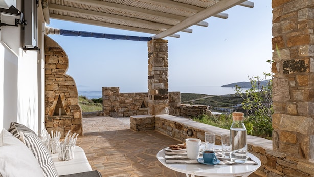 A stone-walled outdoor seating area with a table set for two, overlooking a scenic view. - Kalliston, Romantic Villa with Amazing Sea View (Naxos)