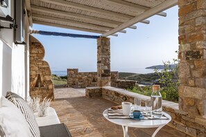 A stone-walled outdoor seating area with a table set for two, overlooking a scenic view. - Kalliston, Romantic Villa with Amazing Sea View (Naxos)