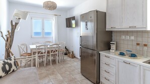 A compact kitchen with a stainless steel refrigerator, white cabinetry, and a dining area with a table and chairs. - Kalliston, Romantic Villa with Amazing Sea View (Naxos)