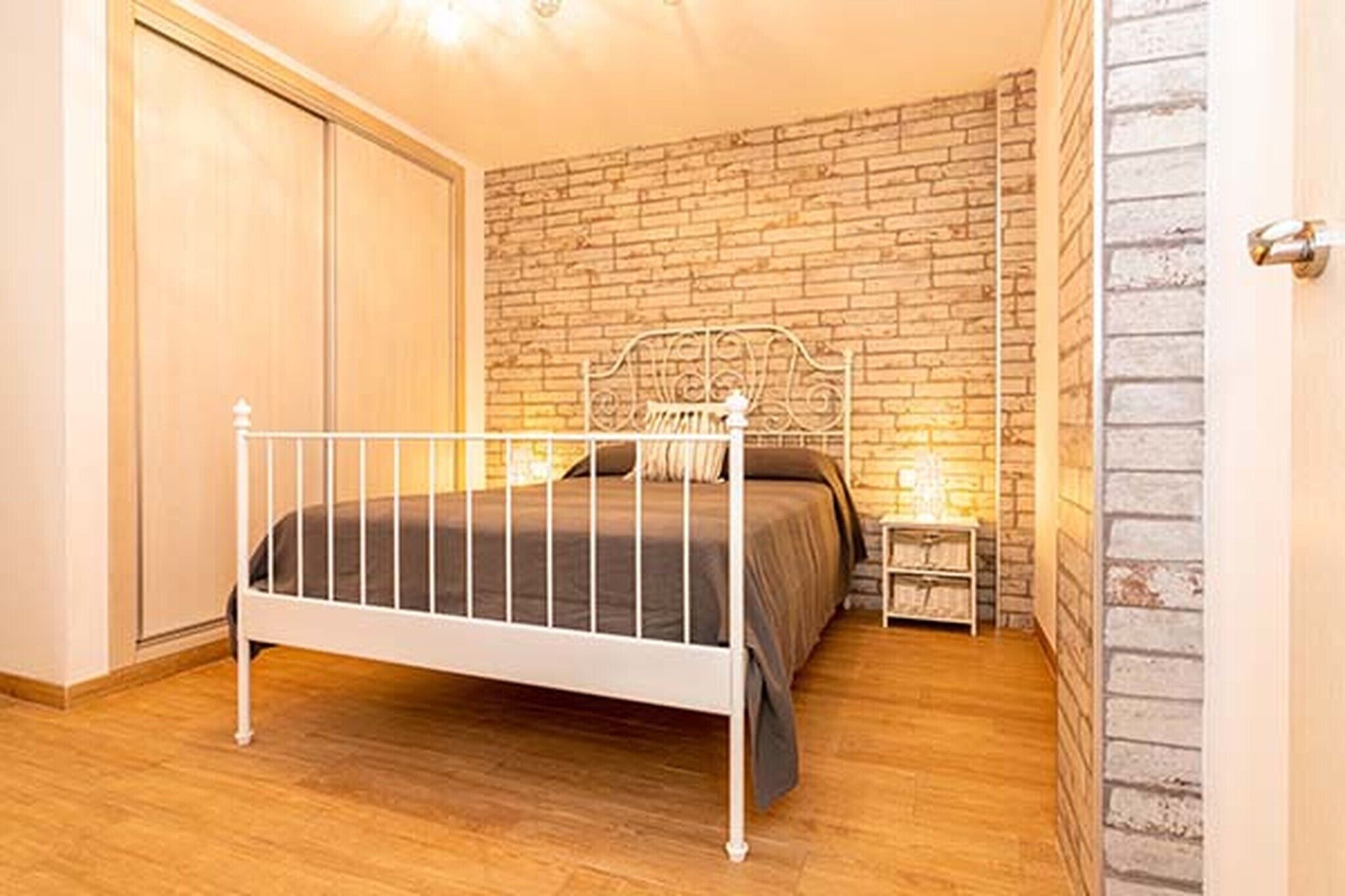A bedroom with a metal bed frame, a brick-patterned wall, and a wooden floor.