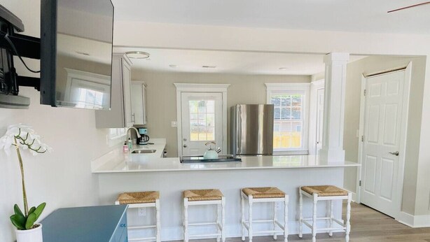 Una cocina moderna con muebles blancos, un refrigerador de acero inoxidable y una barra con taburetes.