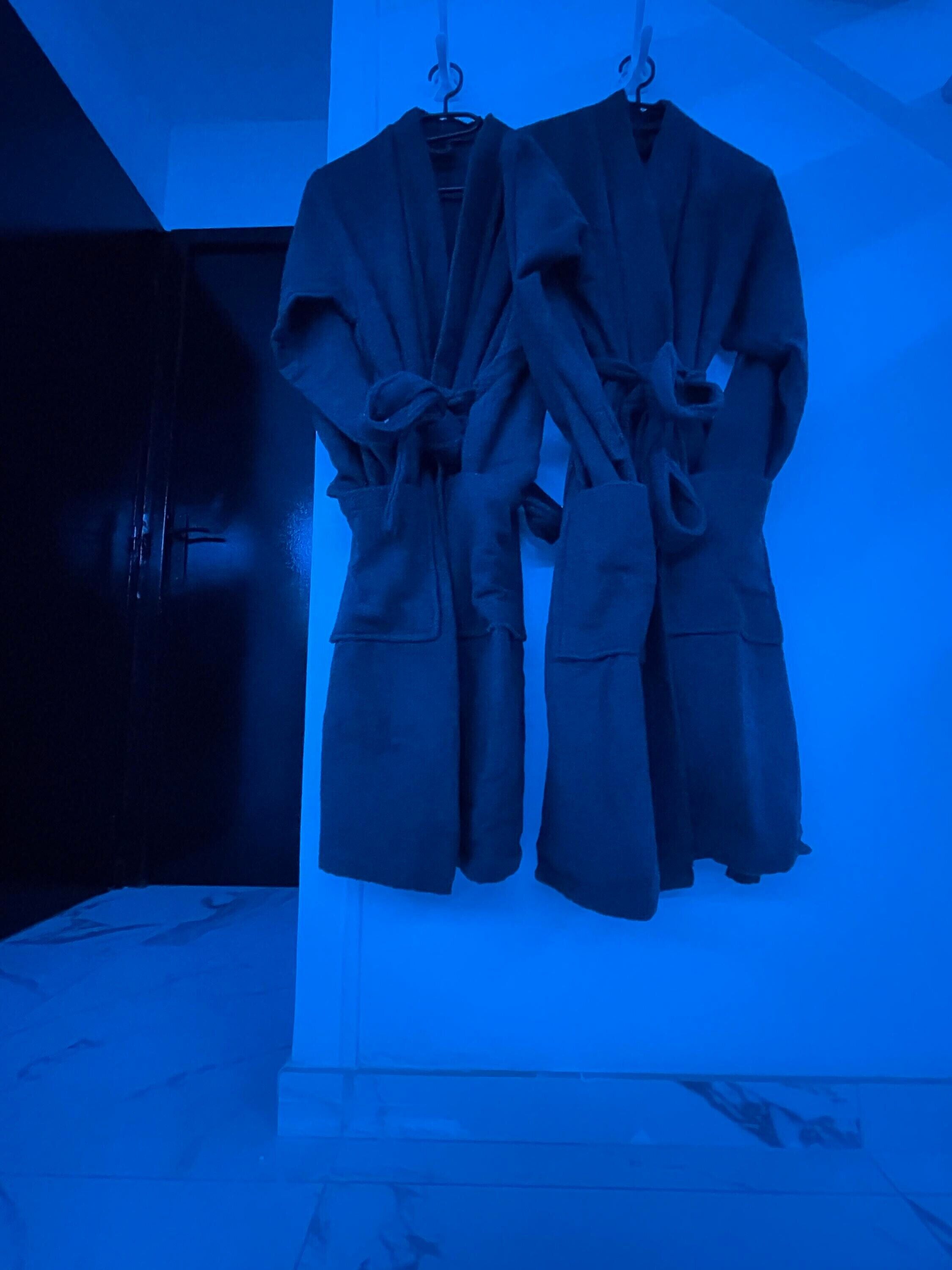 Two bathrobes hanging on a rack in a room with a marble floor.