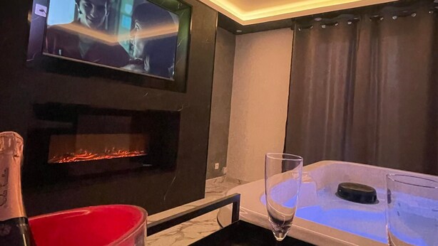 Une pièce avec un téléviseur fixé au mur, une cheminée, une table décorée de pétales de roses et un seau rouge sur lequel est écrit le mot « Cliché ».