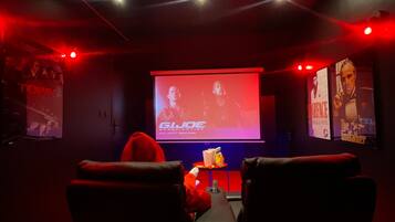 Une salle sombre, éclairée d’une lumière rouge tamisée, un écran affichant le titre d’un film, et une rangée de sièges noirs.