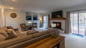 A modern living room with a sectional sofa, a fireplace, a flat-screen TV, and large windows. - Riverwood at Mill Ridge - hot tub, arcades, firepit along Watauga River, walk to pool, tennis (Banner Elk)