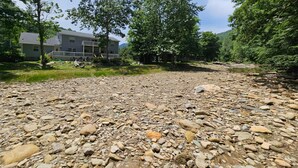 A residential area with a two-story house, a gravel driveway, and a river. - Riverwood at Mill Ridge - hot tub, arcades, firepit along Watauga River, walk to pool, tennis (Banner Elk)