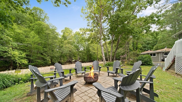 An outdoor seating area with Adirondack chairs arranged around a fire pit. - Riverwood at Mill Ridge - hot tub, arcades, firepit along Watauga River, walk to pool, tennis (Banner Elk)