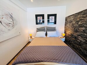 A bedroom with a bed, two bedside tables, a large abstract painting, and a stone wall.