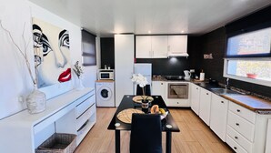 Een moderne keuken met witte kasten, een eettafel met stoelen, een magnetron, een wasmachine en een groot raam.