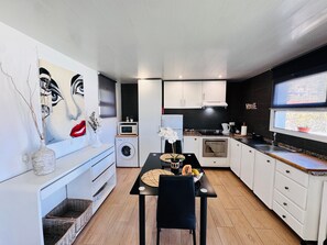 Une cuisine moderne avec des meubles blancs, une table à manger avec des chaises, un four à micro-ondes, un lave-linge et une grande fenêtre.