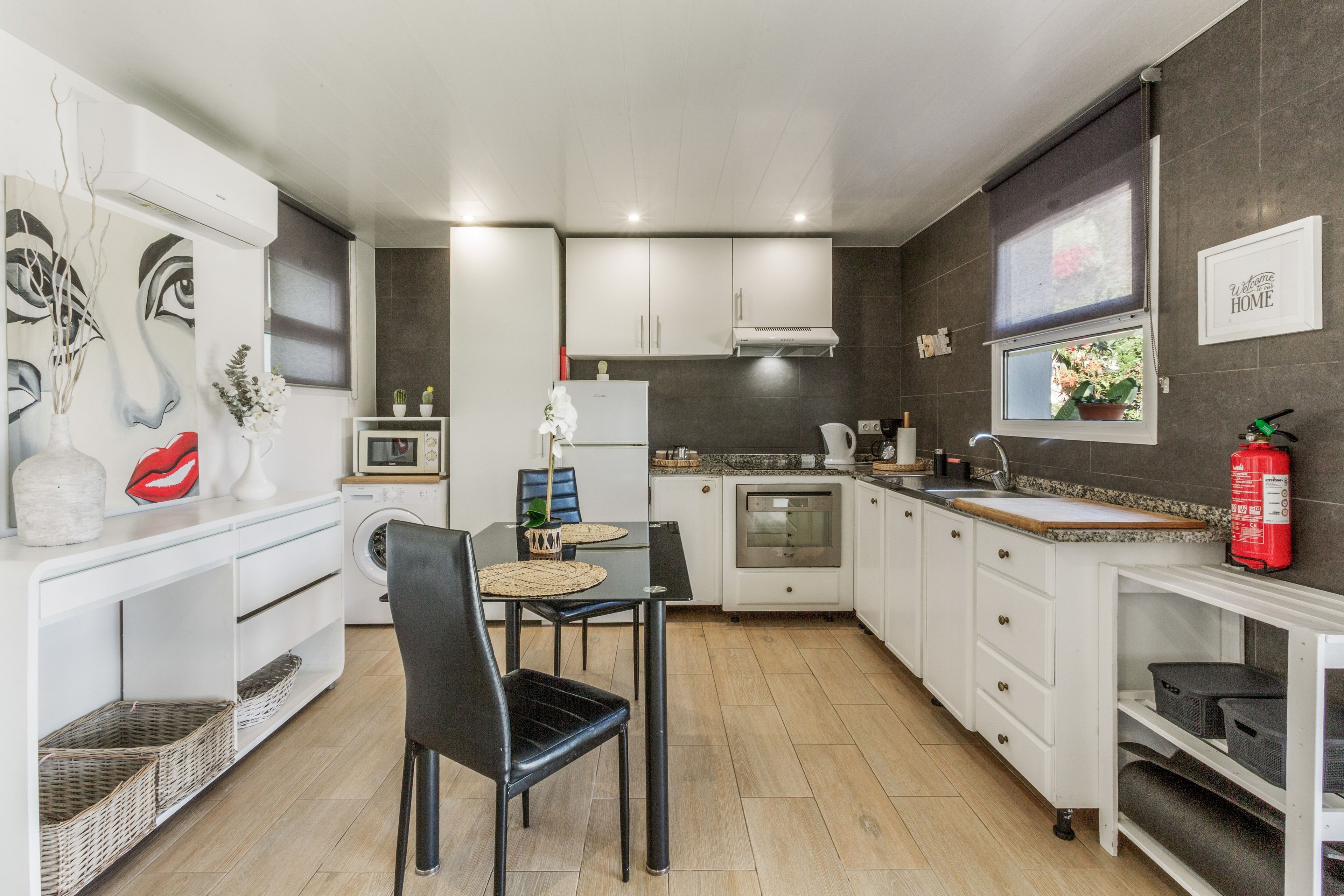 Une cuisine moderne avec des meubles blancs, une chaise noire, un four à micro-ondes, une cuisinière et un extincteur.