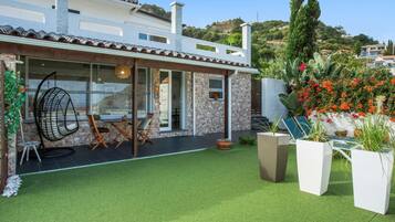 Une maison moderne dotée d’un patio, d’un coin repas avec des chaises et une table, et d’un jardin agrémenté de plantes en pot et de fleurs.