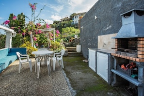 A patio with a round table and chairs, a barbecue grill, and a white wall with a window.