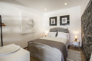 A bedroom with a bed, bedside lamps, a wall-mounted artwork, and a stone accent wall.