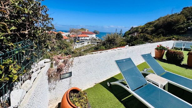 A rooftop terrace with lounge chairs, a view of the sea, and a building with a red roof. - Studio Matilde & Joaquim – Panoramic Sea View (Porto da Cruz)