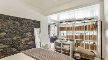 A bedroom with a stone wall, a bed, a desk, and a bookshelf.