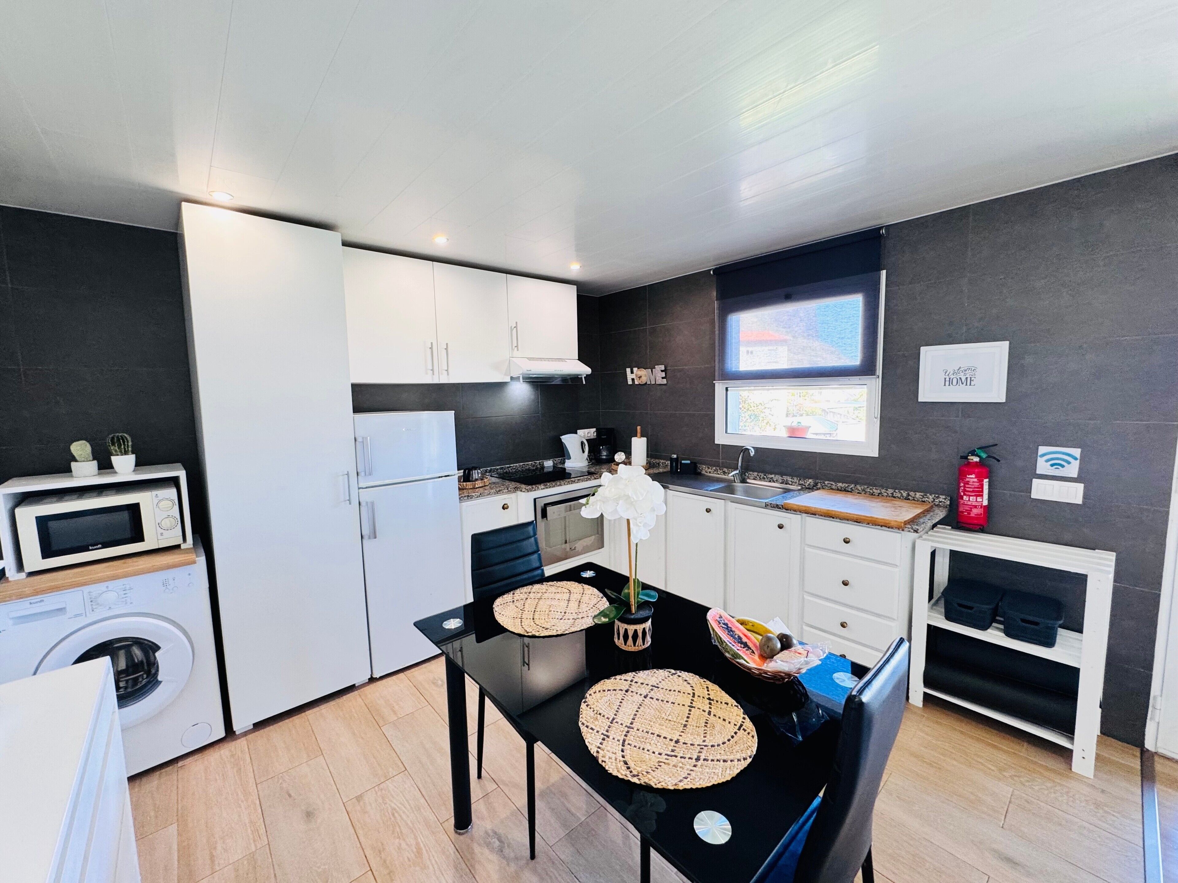 A compact kitchen with white appliances, a dining table with placemats, and a window with a view.
