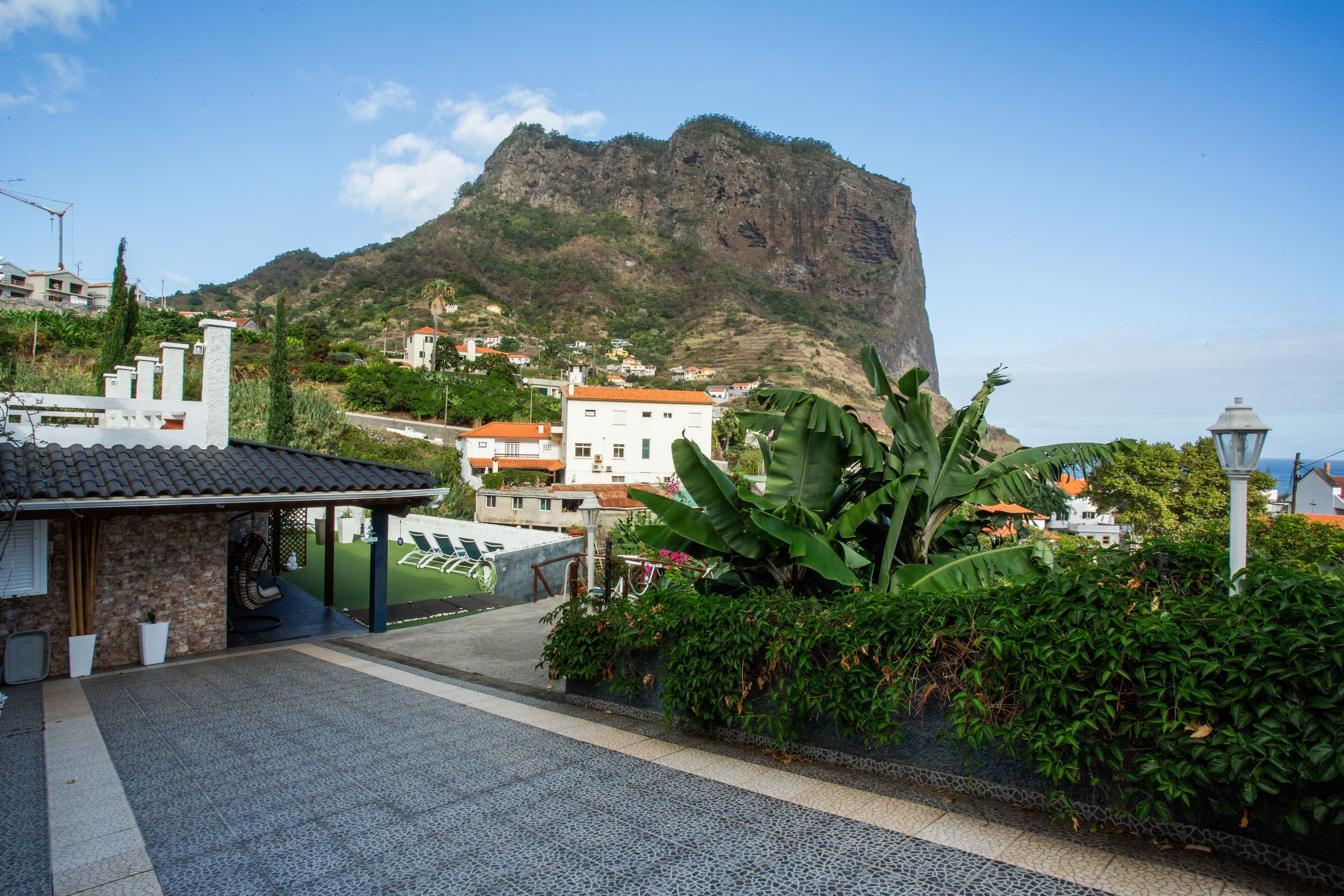 A residential area with a prominent mountain in the background, a paved walkway, and lush greenery.