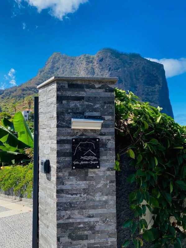 A stone wall with a plaque reading 'Villa Mistral & Joaquim' and a mountain in the background.