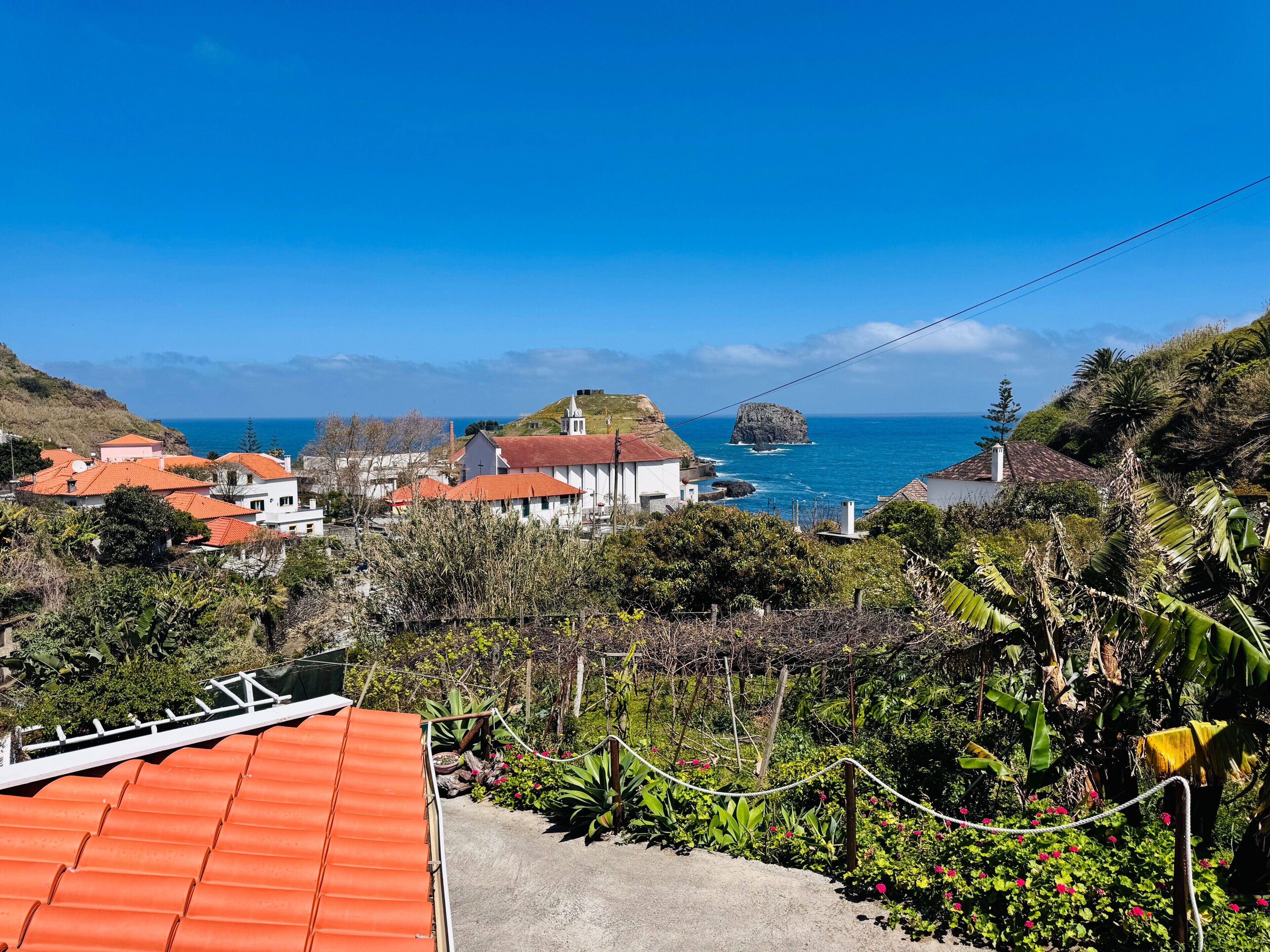 Uma vila costeira com casas, uma igreja e um afloramento rochoso no mar.