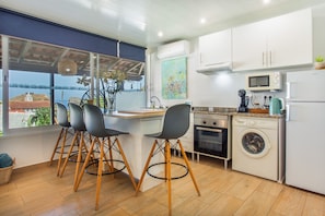 A modern kitchen with a dining area, a washing machine, and a view of the sea. - Villa Matilde e Joaquim, Sea View and Nature (Porto da Cruz)