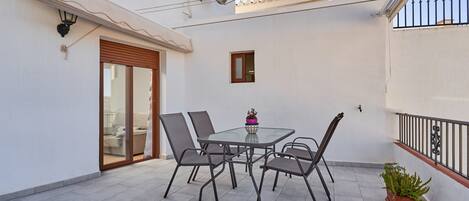 A balcony with a glass table and chairs, a potted plant, and a sliding glass door.