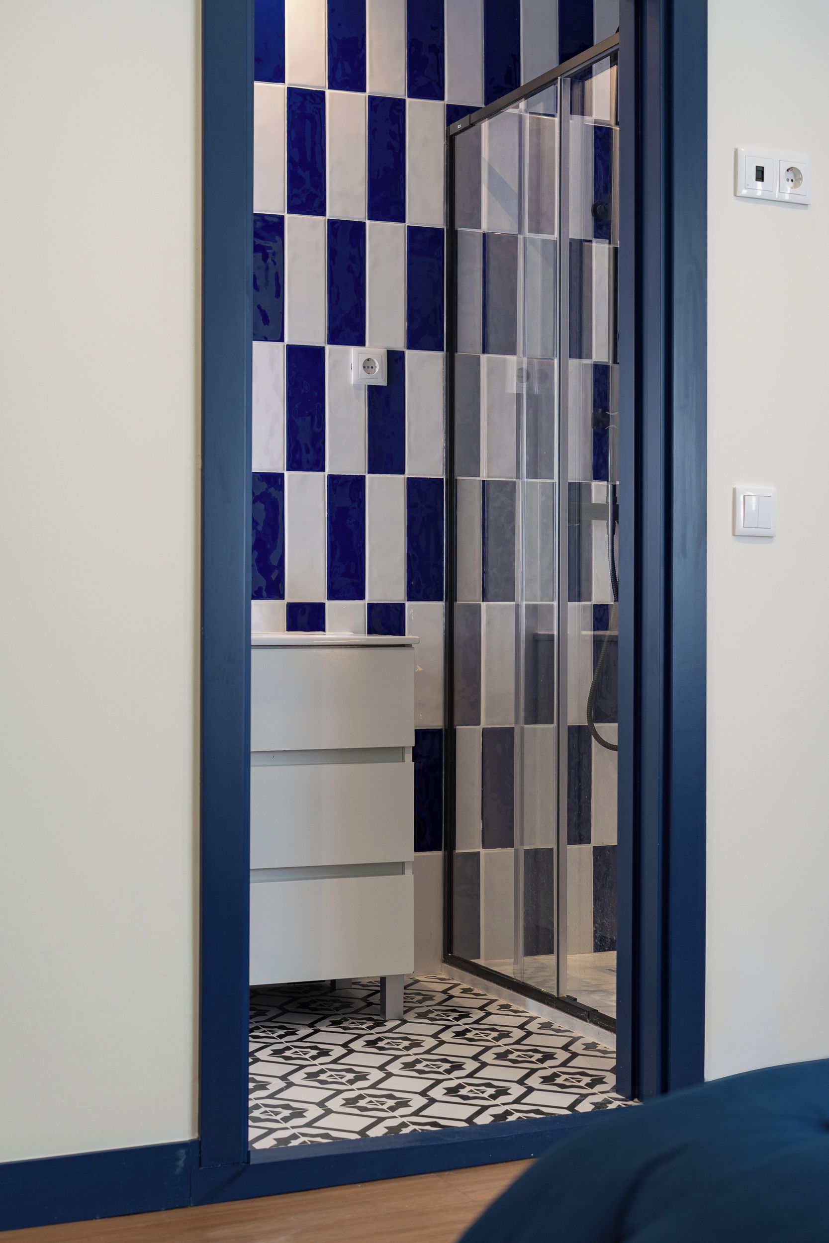 Casa de banho com parede de azulejos xadrez, divisória de chuveiro em vidro e chão estampado.
