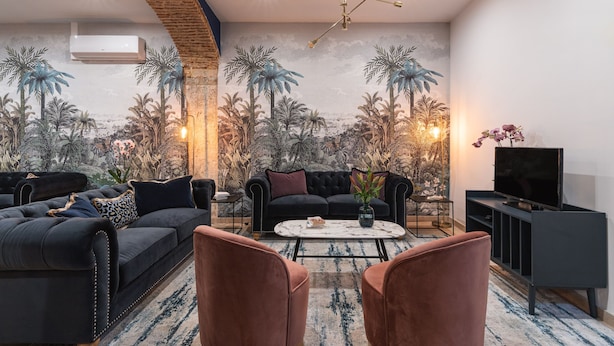 A modern living room with a mural of tropical scenery, a black sofa set, a coffee table, and a TV stand. - Succeed Terreiro do Paço Suites (Lisbon)