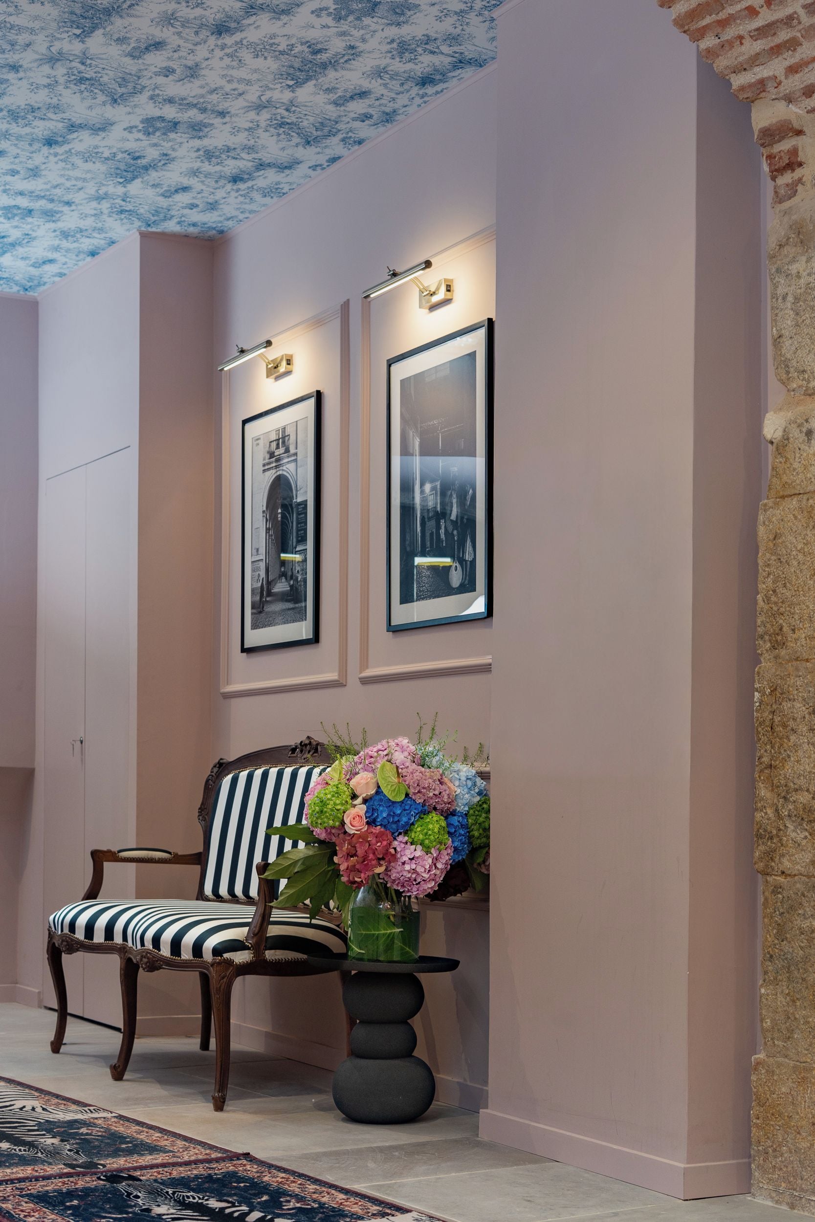 A room with a chair, a table with a vase of flowers, and two framed pictures on the wall.